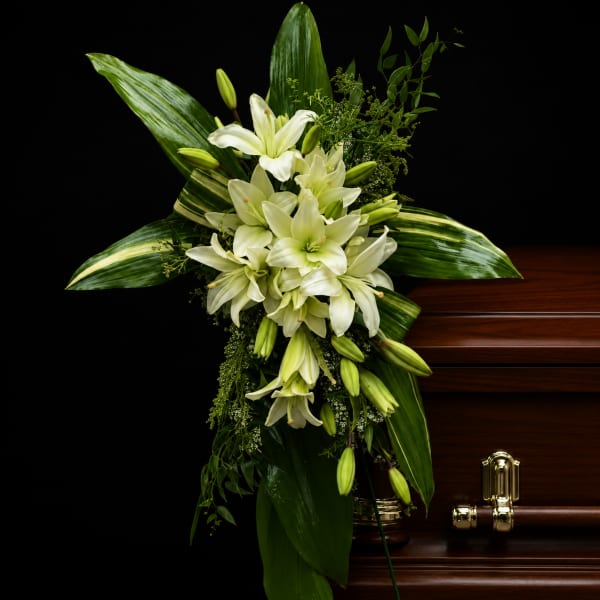 White lilies arranged in a dark wood casket with green foliage
