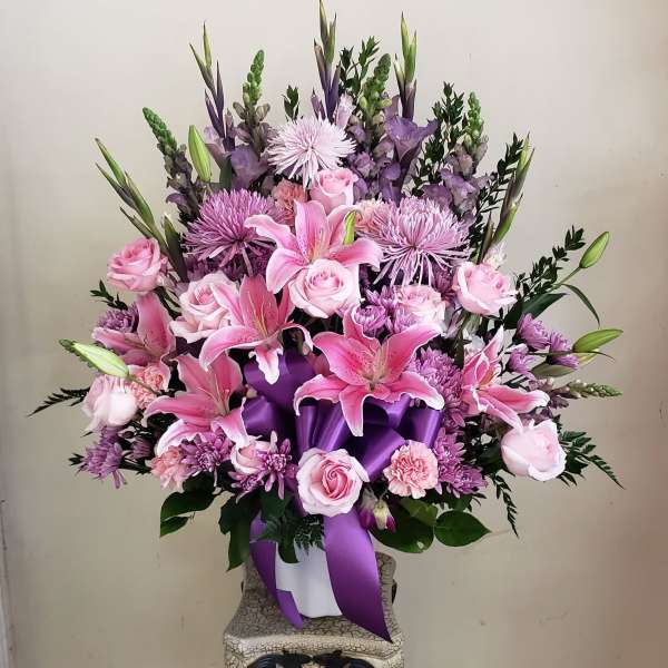 Pink and purple floral arrangement in a white container with a purple ribbon
