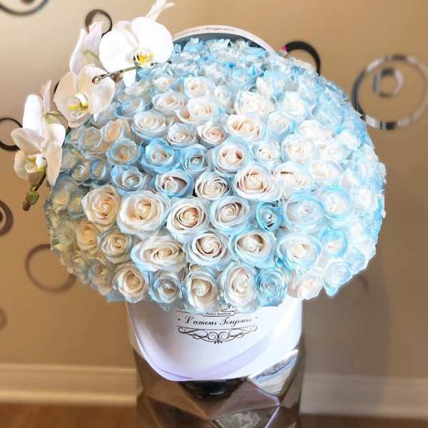 Round hatbox filled with cream and light blue roses topped with a spray of white orchids