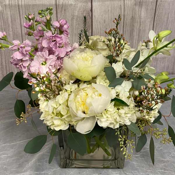 White and pale pink floral arrangement in a square glass vase