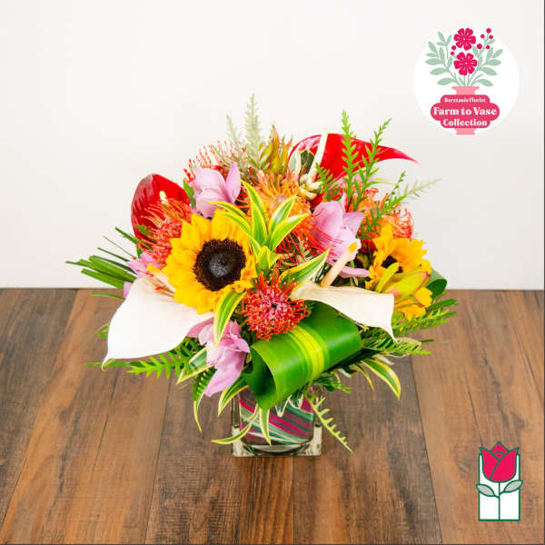 Tropical bouquet with sunflowers, white calla lilies, and pink orchids in a square vase