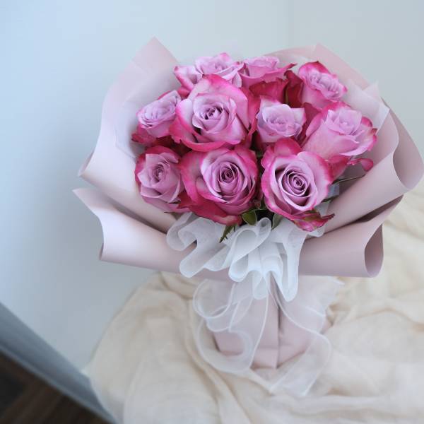 Bouquet of pink roses wrapped in pale pink paper with a white ribbon