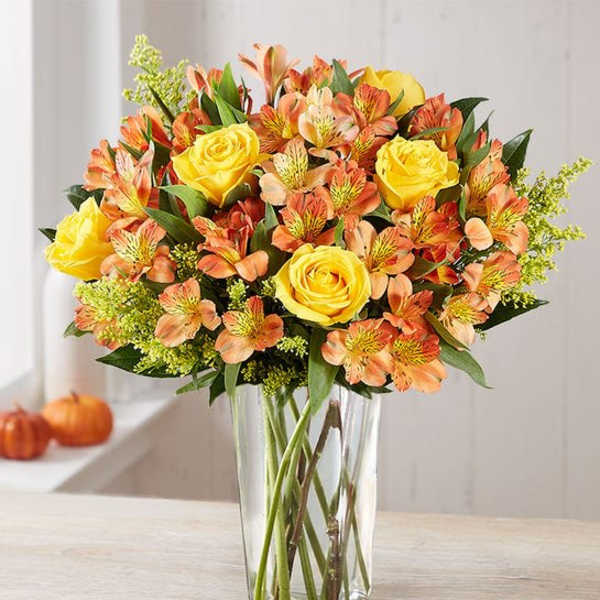 Yellow roses and orange alstroemeria in a clear glass vase