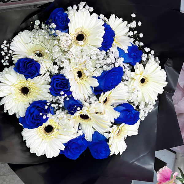 Bouquet of white gerbera daisies and blue roses wrapped in black paper