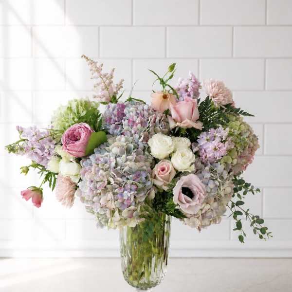 Pastel bouquet of hydrangeas, roses, and anemones in a clear glass vase