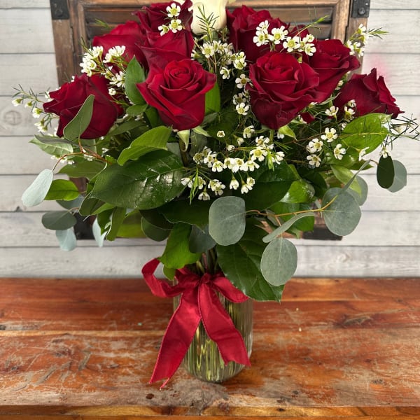 Red roses and white filler flowers in a glass vase with a red ribbon