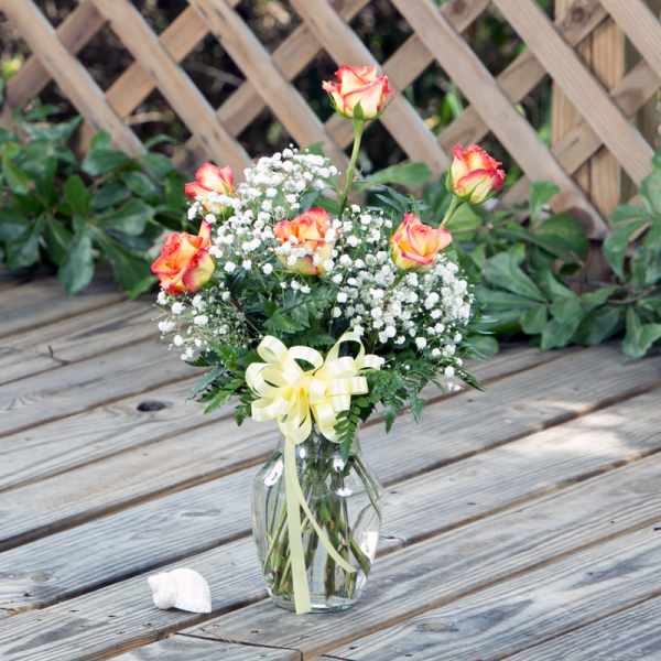 Bouquet of orange-edged roses in a glass vase with a yellow ribbon