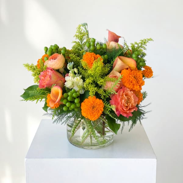 Mixed bouquet of orange and pink flowers in a clear glass vase