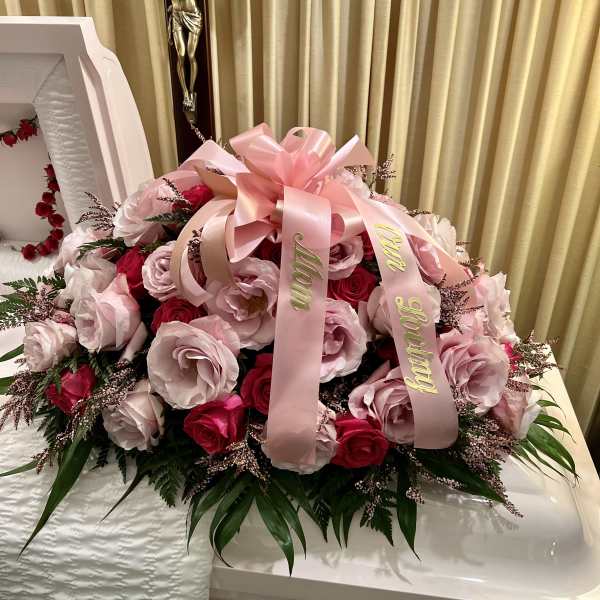 Pink and red rose arrangement on a white casket with a pink ribbon.