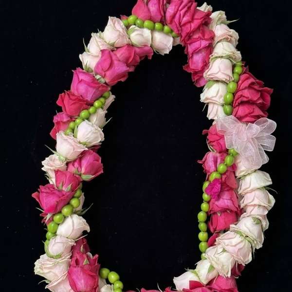 Pink and white rose lei with green beads on a black background