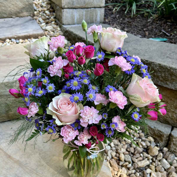 Bouquet of pink roses, carnations, and purple daisies in a glass vase