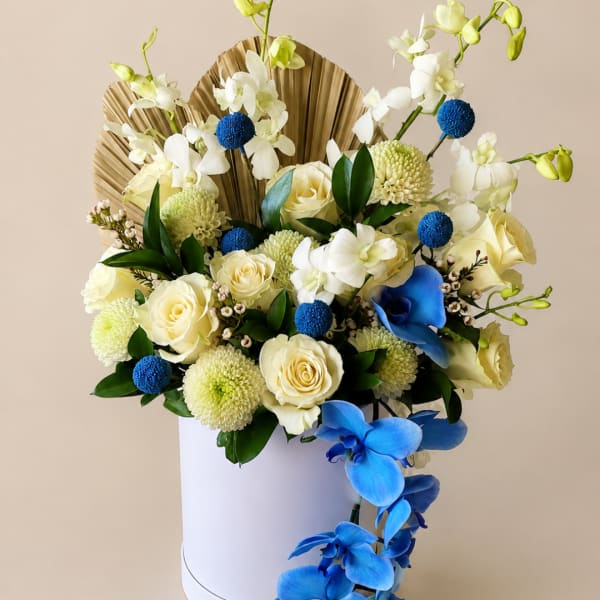 White and blue floral arrangement in a white box with fan-shaped backing