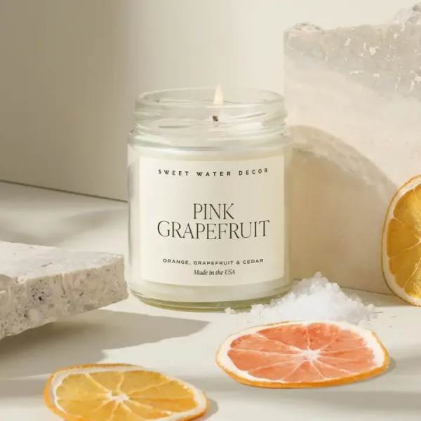 A lit pink grapefruit candle in a glass jar with dried citrus slices nearby.