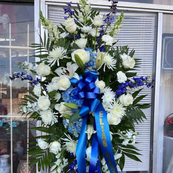Tall white and blue funeral spray on an easel with a blue ribbon