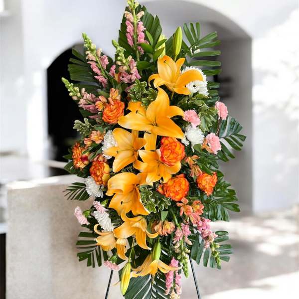 Standing floral spray with orange lilies and pink blooms on a metal easel