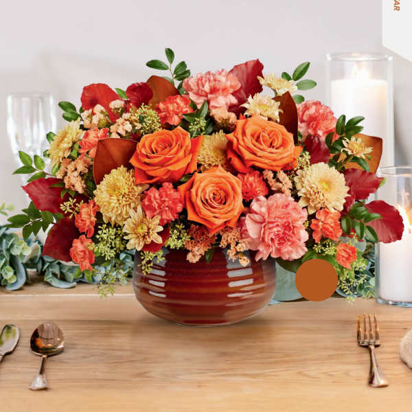 Orange and pink floral arrangement in a round vase on a table