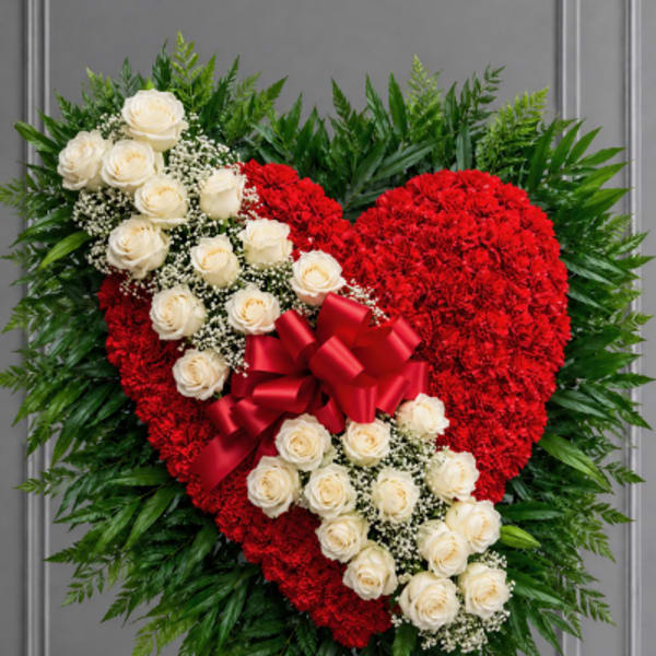 Heart-shaped red floral tribute with white roses and a red bow on an easel
