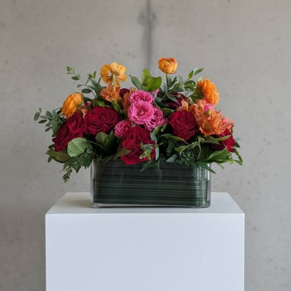 Mixed bouquet of red, pink, and orange flowers in a rectangular glass vase