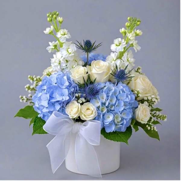 Blue hydrangeas and white roses arranged in a white box with a ribbon