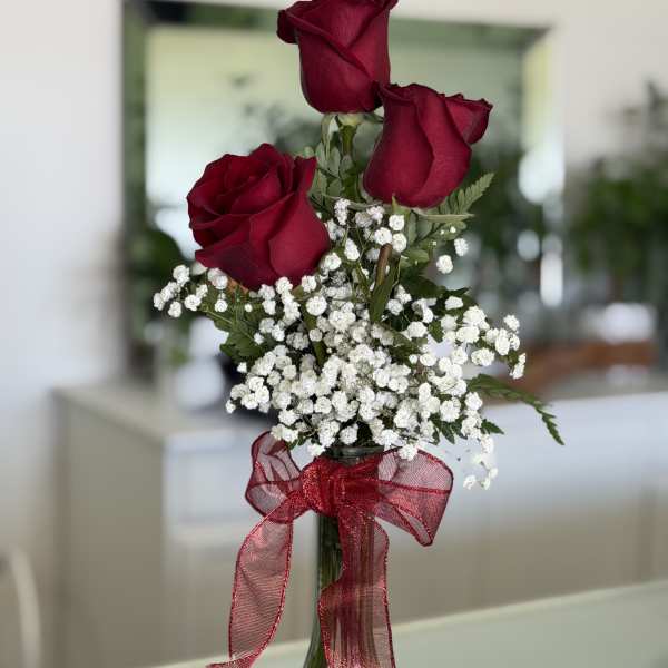 Three red roses in a glass vase with white baby's breath and a red ribbon