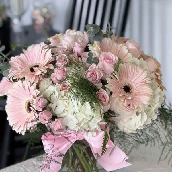 Pink gerbera daisies and roses in a glass vase with a pink ribbon