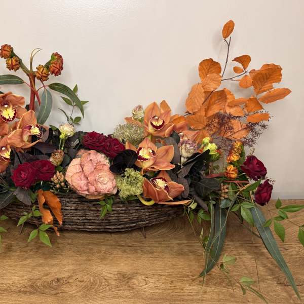 Low floral centerpiece in a woven basket with orange orchids and red roses
