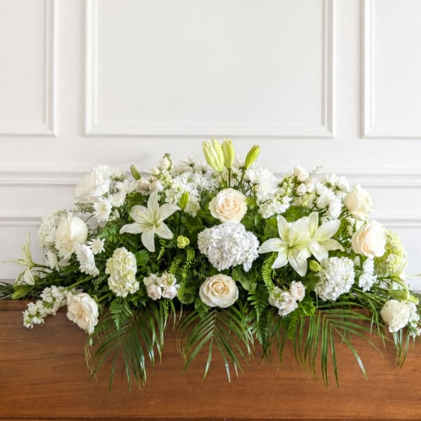 White floral arrangement with lilies, roses, and hydrangeas on a wooden surface