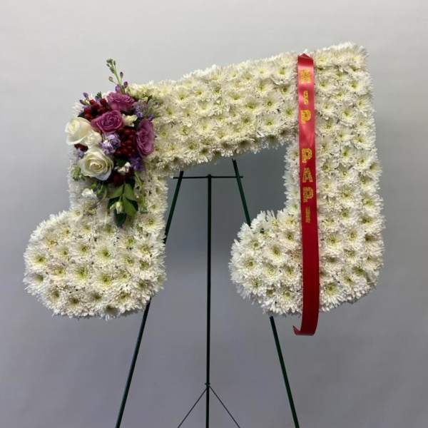 Large white floral funeral wreath on an easel with a red ribbon