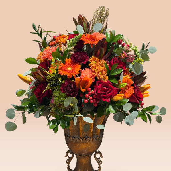 Mixed bouquet of orange, red, and pink flowers in a bronze urn vase
