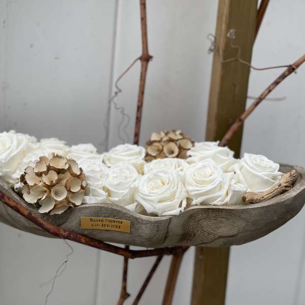 White roses arranged in a shallow wooden vessel with dried accents
