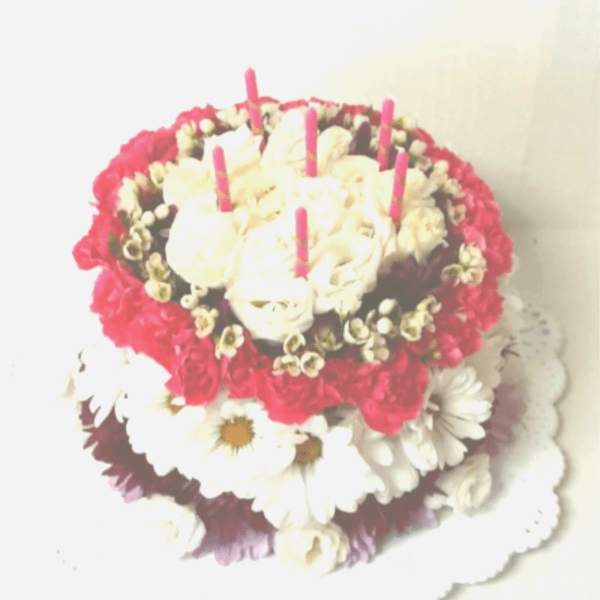 Round floral cake with white roses, daisies, and pink candles
