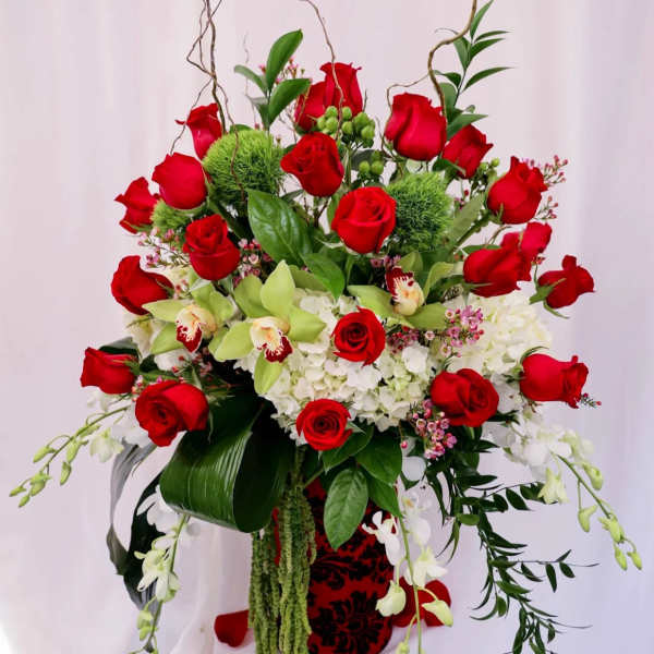 Tall bouquet of red roses, white orchids, and white hydrangeas in a decorative vase