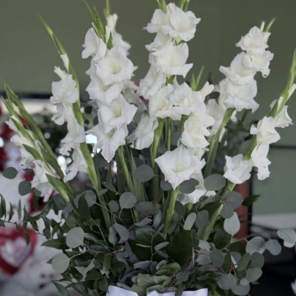 White gladiolus arrangement in a clear glass vase with a white ribbon