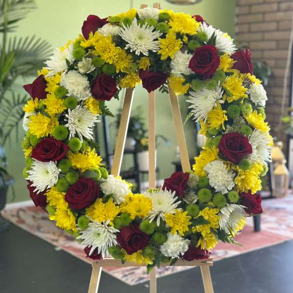 Circular floral wreath with red roses, white chrysanthemums, and yellow blooms on an easel