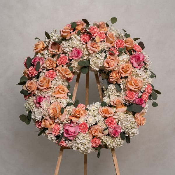 Large circular floral wreath on a wooden stand with pink and peach blooms