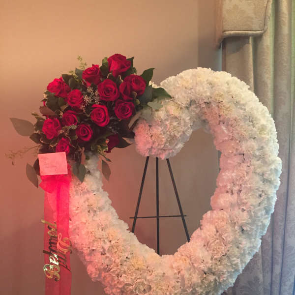 Heart-shaped white floral wreath with red roses and a pink ribbon