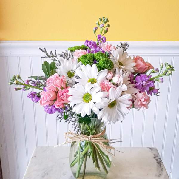 Mixed bouquet of white daisies, pink roses, and purple flowers in a glass vase