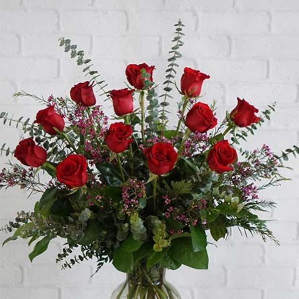 Red roses arranged in a clear glass vase with eucalyptus and filler flowers