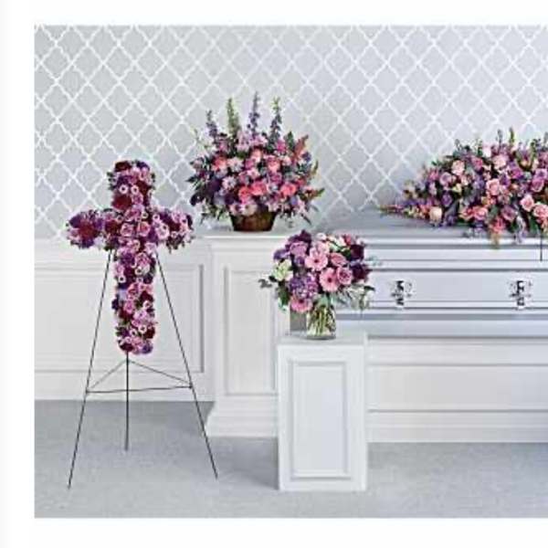 Multiple pink and purple floral funeral arrangements around a white casket