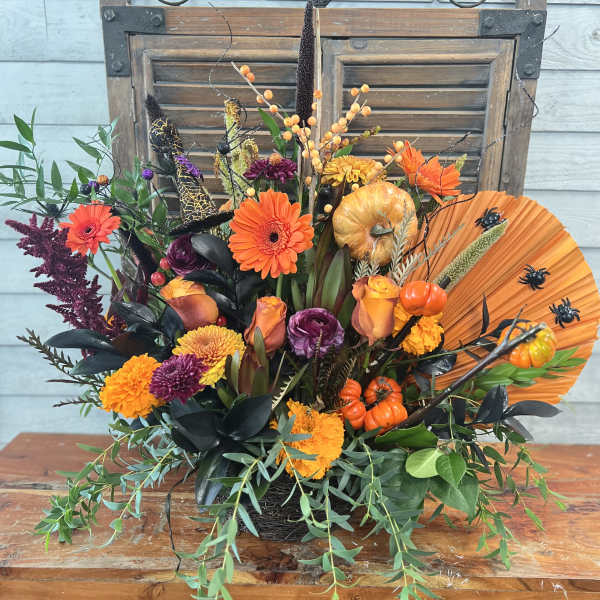 Autumn floral arrangement with orange and purple blooms, pumpkins, and a fan accent