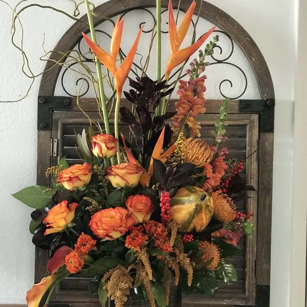 Orange and yellow floral arrangement in a dark vase with tall tropical blooms