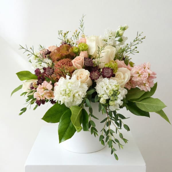 Mixed bouquet of roses, hydrangeas, and small blooms in a white vase