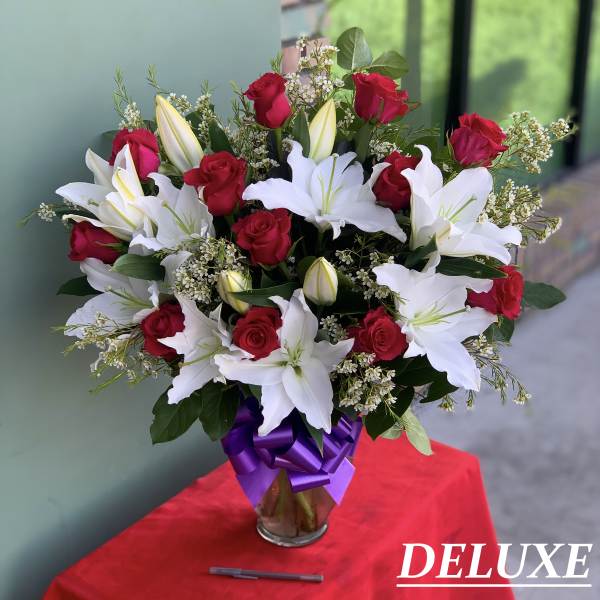 Bouquet of red roses and white lilies in a glass vase with a purple ribbon