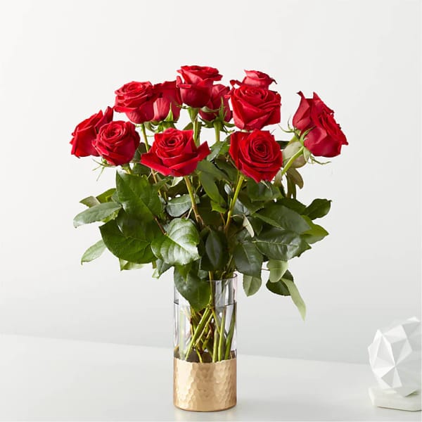Tall arrangement of red roses in a clear glass vase with a gold base