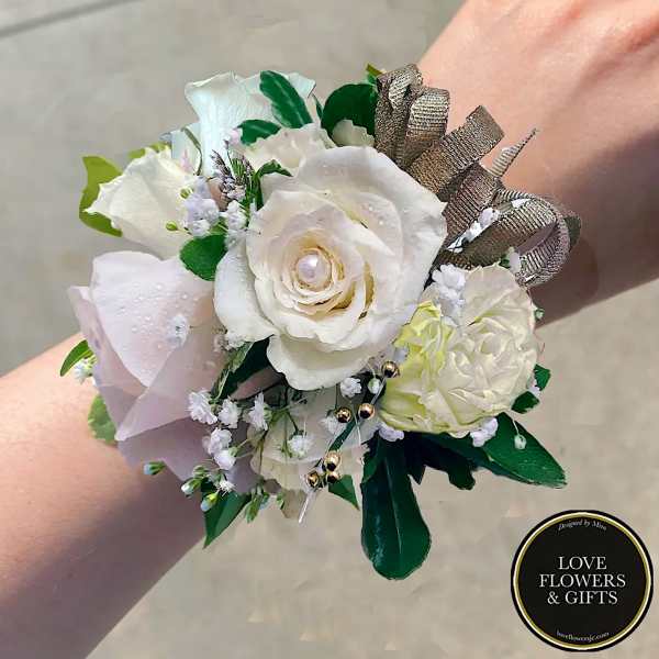 Wrist corsage of white and pale blush roses with baby’s breath and gold ribbon on a person’s wrist.