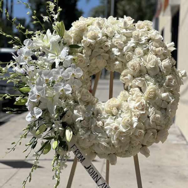 White floral wreath on an easel with a ribbon reading "FROM JOHN AND NICOLE"