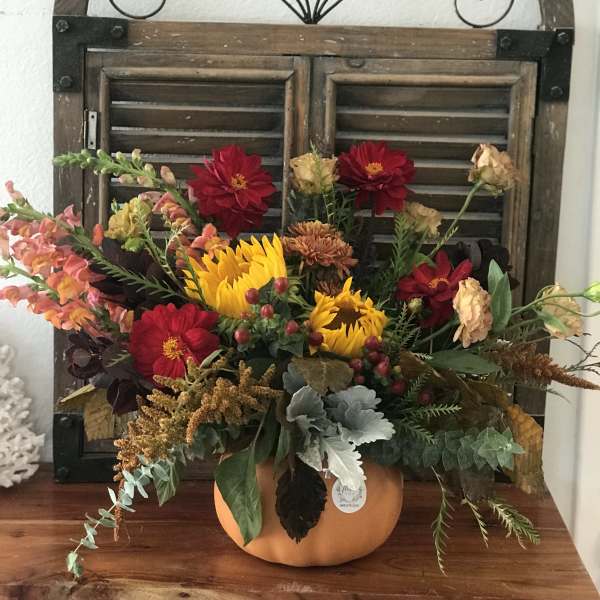 Fall floral arrangement in a pumpkin container with sunflowers and red blooms