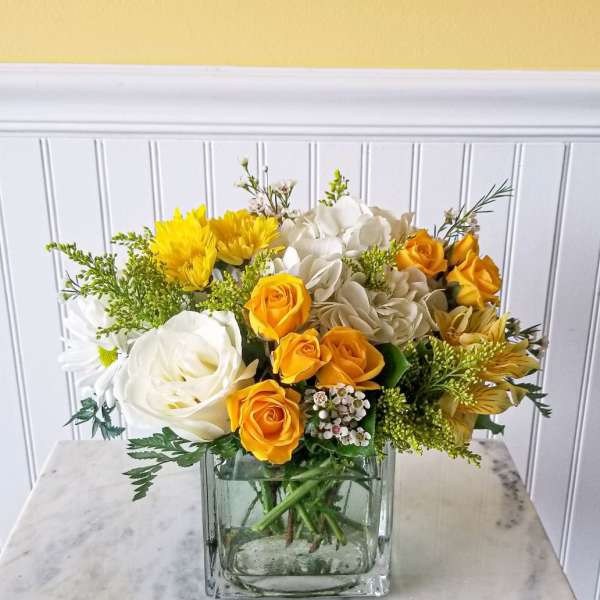Yellow and white flower arrangement in a square glass vase