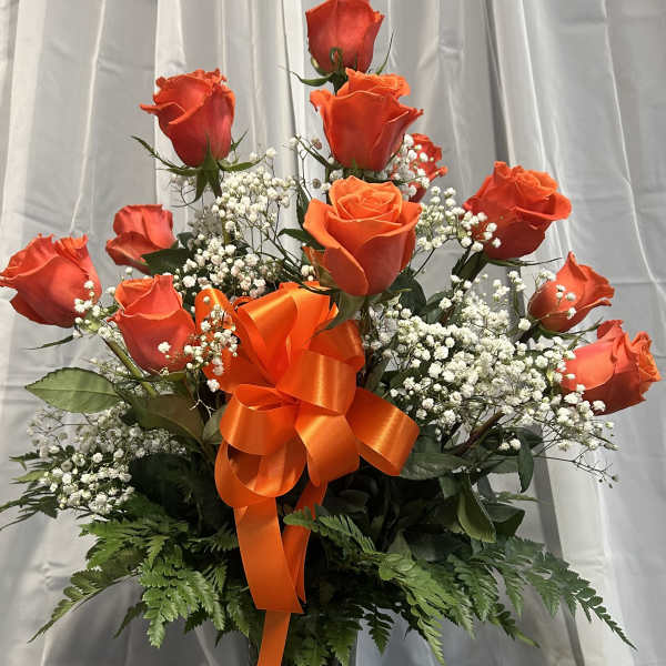 Orange roses in a glass vase with a large orange ribbon and white filler flowers.