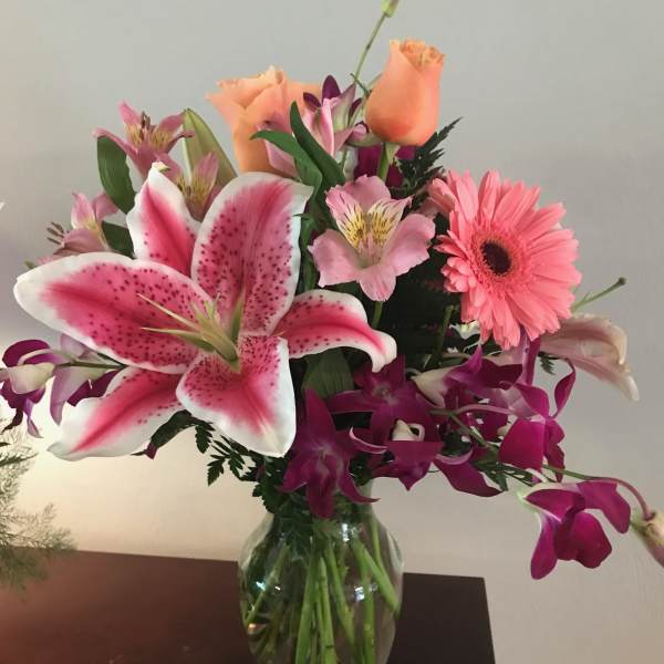 Mixed bouquet of pink lilies, roses, and a gerbera daisy in a glass vase